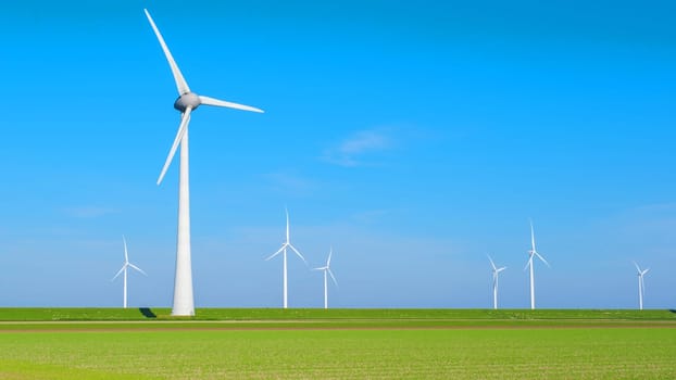 A scenic view of a wind farm in the Netherlands Flevoland, with several windmills turning gracefully in the background against a clear sky. green farmland with windmill turbines