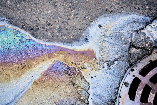 An oil slick of gasoline or oil on an asphalt road flows into a storm drain.