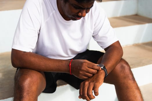 Close up Asian young athlete sport runner black man wear modern time smart watch he sitting resting before training running at the outdoor street health park, healthy exercise before workout concept