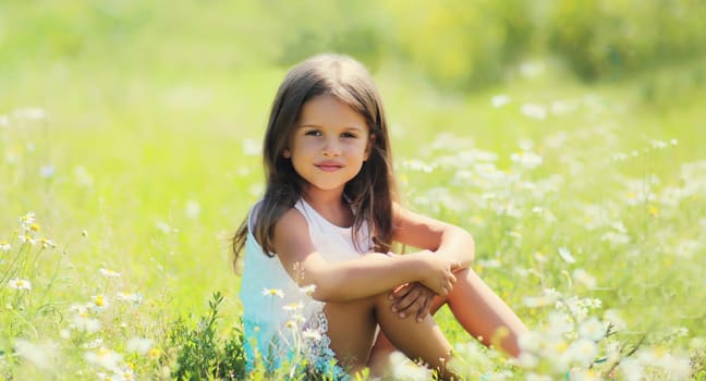 Portrait of happy little girl child sitting on grass in sunny summer park