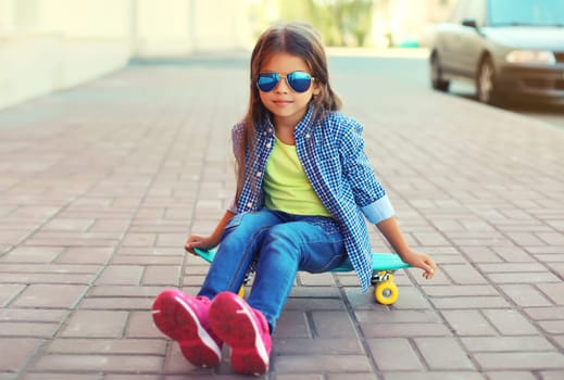 Portrait of stylish little girl child posing with skateboard on city street