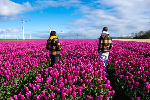Two individuals peacefully walk through a vibrant field of purple tulips, surrounded by the beauty of nature in full bloom under a clear sky. a diverse couple of men and women ina flower field