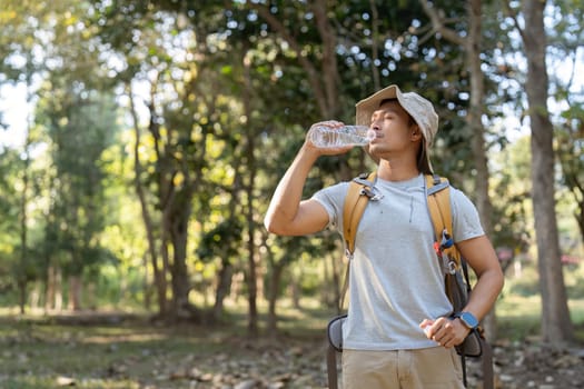 Traveler hiking man carrying a backpack on the back and walking in national park. man asian is rest by drink water.