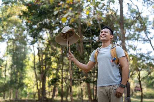 Young man asian trekking among trees with backpack, young man enjoy alone in forest. Camping, hiking, travelling, search for adventure concept.