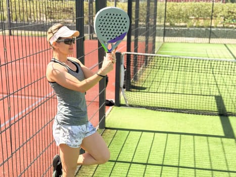 Portrait of active emotional woman playing padel tennis on open court in summer, swinging racket to return ball over net .. High quality photo