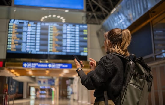 Young Asian woman in international airport looking at flight information board, checking her flight.