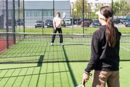 positive mother and daughter standing on court with padel rackets. High quality photo