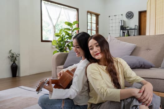Asian young lover lesbian couple playing guitar with relax and happy moment in living room LGBT relationship in lifestyle concept.