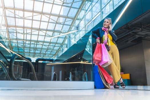Mature woman talking smartphone with shopping bags in the mall. High quality photo