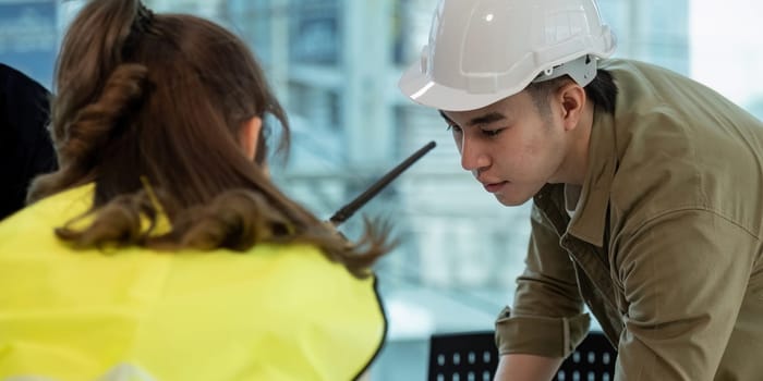 Teamwork in construction site, civil engineer or professional foreman in safety helmet hard hat using blueprint in while standing at industrial factory, teamwork concept.