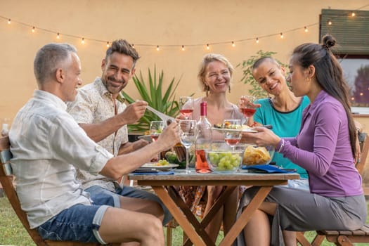 Friends eating and drinking happy smiling and laughing in the patio. Middle-aged cheerful people around the table on summer vacations. High quality photo