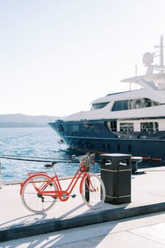 Two-wheeled bicycle with a basket is fastened to a pole on the boardwalk near a moored yacht. High quality photo