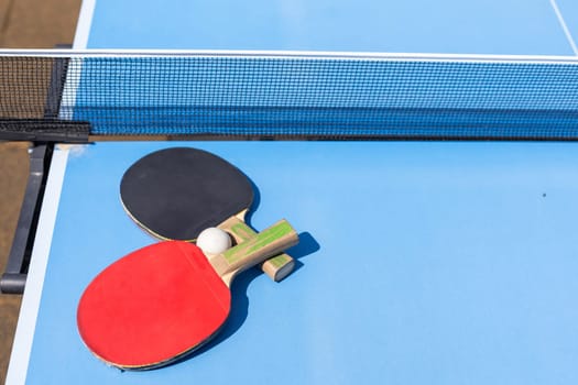 Two table tennis or ping pong rackets and ball on blue table with net. High quality photo