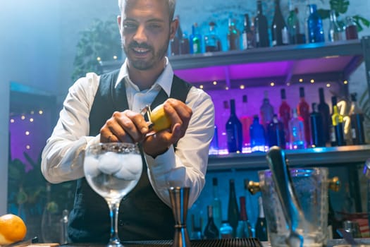 Happy attractive barman in a white shirt and black apron making cocktail at party in nightclub. Nigh life. High quality photo