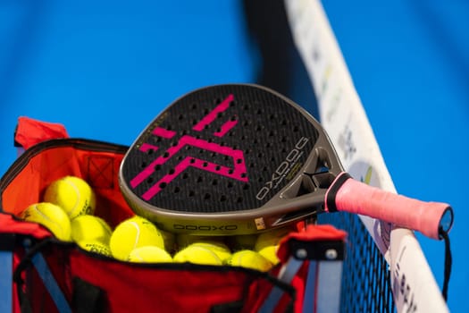 Kyiv, Ukraine, April 18, 2024. Black professional paddle tennis racket and ball with natural lighting on blue background. Horizontal sport theme poster, greeting cards, headers, website and app. High quality photo