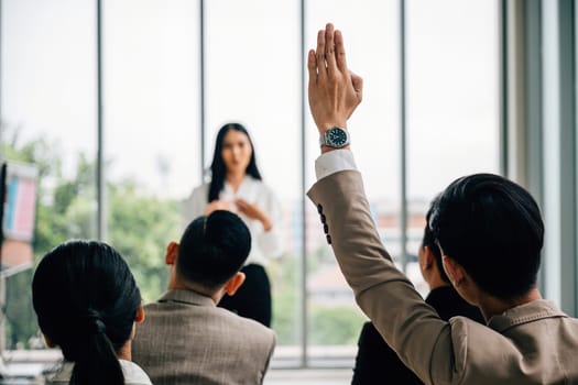 In a seminar classroom at a conference, a large group raises hands in participation. The engaged audience holds the answers, symbolizing collaborative learning.