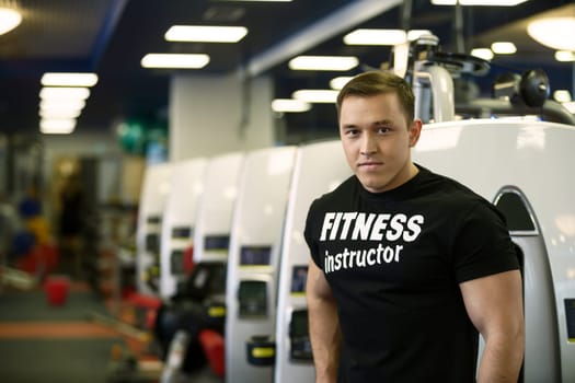 Fitness instructor posing on backdrop of sports equipment