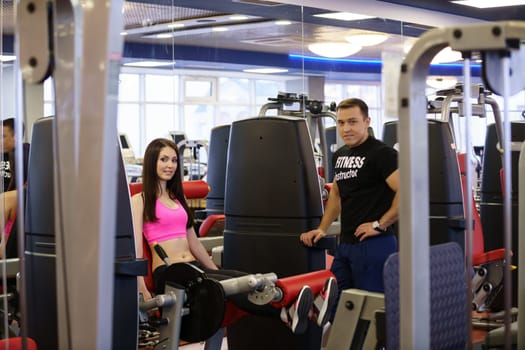 In gym. Fitness instructor and pretty girl posing at camera