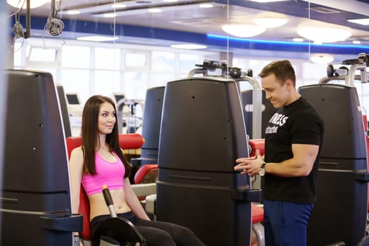 Fitness instructor helps girl to choose right exercise