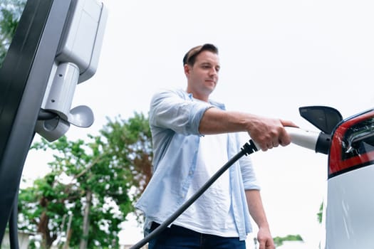 Eco-friendly conscious man recharging modern electric vehicle from EV charging station. EV car technology utilized as alternative transportation for future sustainability. Synchronos