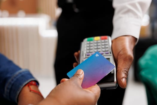 Close up of customer hand making NFC transaction holding credit card paying in hotel with contactless payment method. Traveler paying for hospitality services, electronic money, e-pay