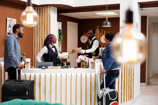 African American couple man an woman standing at hotel reception checking in at reception, waiting for room key or access card. Front desk staff managing guest check-in or check-out process