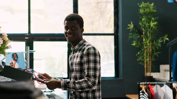 African american man shopping for formal wear, checking fashionable tie material in clothing store. Shopaholic customer buying trendy clothes and stylish accessories in modern boutique