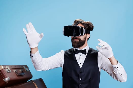 Classy bellboy using virtual reality on headset, symbolizing modern hospitality industry in studio. Hotel porter wearing white gloves and vr glasses, providing luxury services.