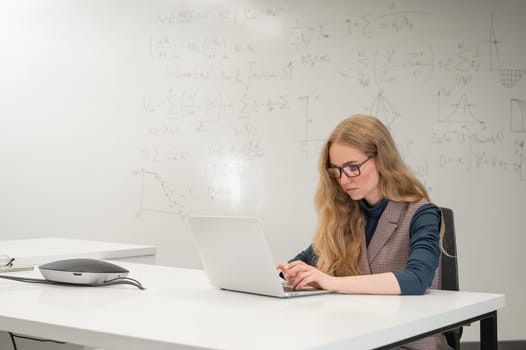 Caucasian woman scientist typing on laptop. White board with formulas