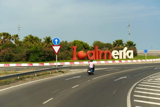 Almeria, Spain - May 25, 2023: A man wearing a helmet is riding a motorcycle down a street lined with buildings, passing by a sign. The scene captures the movement and urban setting.