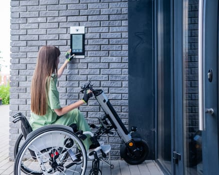 A woman in a wheelchair with an assistive device for manual control enters the entrance. Electric hand bike