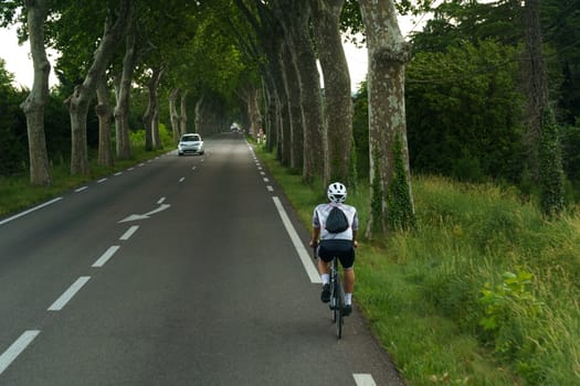 Nimes, France - May 30, 2023: A man is cycling down a street lined with tall trees on a sunny day.