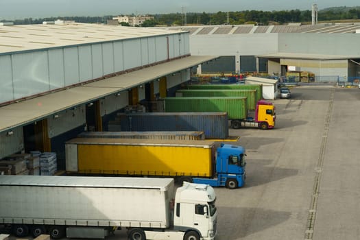Trucks docked at a cargo bay with colorful freight containers, facilitating logistics and transport at a warehouse facility.