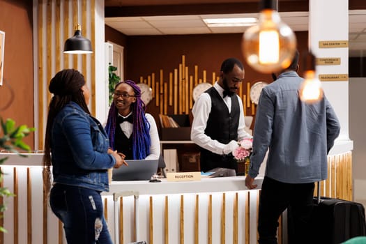 Friendly smiling front desk staff welcoming visitors at reception area of hotel. Smiling African American receptionist giving arriving guests information. People checking in at resort