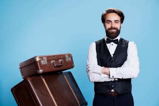 Hotel bellhop with luggage in studio, providing assistance to people and helping with trolley bags. Professional doorman or bellboy with suit and tie feeling confident on camera.