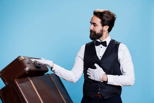 Male bellhop points left and right to create new advertisement, indicating direction sideways while he wears formal attire. Young classy doorman presents ad over blue background.
