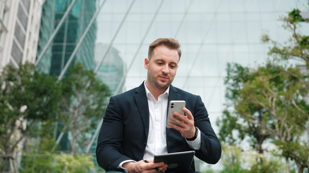 Front view of businessman sitting at park while talking to investors about marketing strategy. Caucasian executive manager looking increasing sales or successful project at eco city. Lifestyle. Urbane