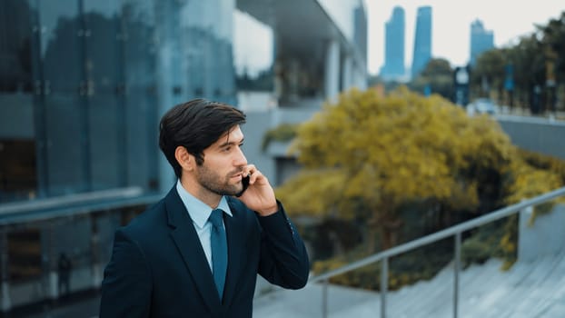 Skilled caucasian project manager calling phone while walking at city with blurred background. Skilled businessman using smart phone talking to project manager with blurred background. Exultant.