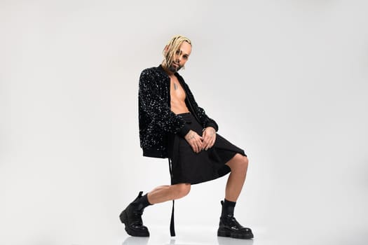 Full length gay man wearing women clothing dancing. Brazilian homosexual male wearing black skirt and boots posing in photo studio on white background. Bearded gay with make up. Full length