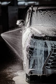 Man applying foam to black car in car wash. Vertical photo
