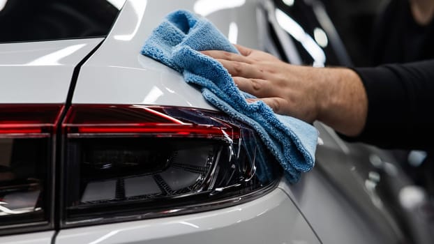 A mechanic wipes the body of a white car with a microfiber cloth