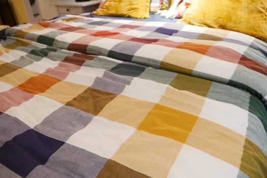 a bed with a colorful plaid comforter and pillows in shades of Purple, Orange, and Yellow
