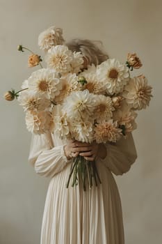 A woman in a white dress is holding a bouquet of white flowers in front of her face, showcasing a beautiful arrangement of petals and twigs in a beige vase