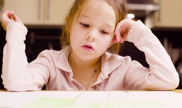A girl drawing pastel crayons on paper at a table in a room