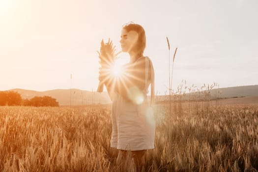 A woman is holding a bunch of wheat in her arms. The wheat is dry and brown, and the woman is wearing a white dress. The scene is set in a field, and the woman is posing for a photo