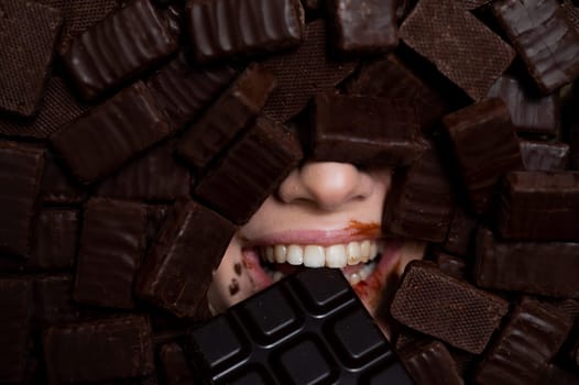 The face of a caucasian woman surrounded by chocolates. The girl eats a bar of chocolate