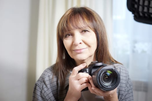 Senior old elderly woman with black camera with a large lens indoors in the studio. Professional photographer. Age Hobby