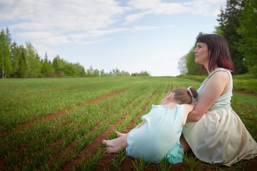 Happy mother and daughter enjoying rest, playing and fun on nature in green field. Woman and girl resting outdoors in summer or spring day