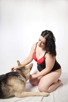Portrait of attractive thick woman in red black swimsuit with big dog shepherd on white background. Body positive, selfie of Funny plus size model