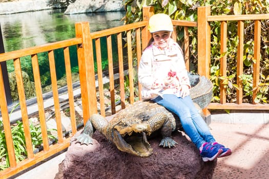 little girl at the zoo with the monument of a crocodile.